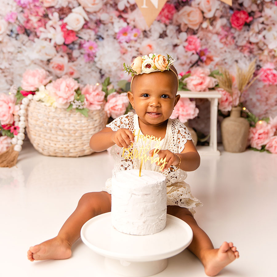 baby with floral headband and lace outfit eating first birthday cake