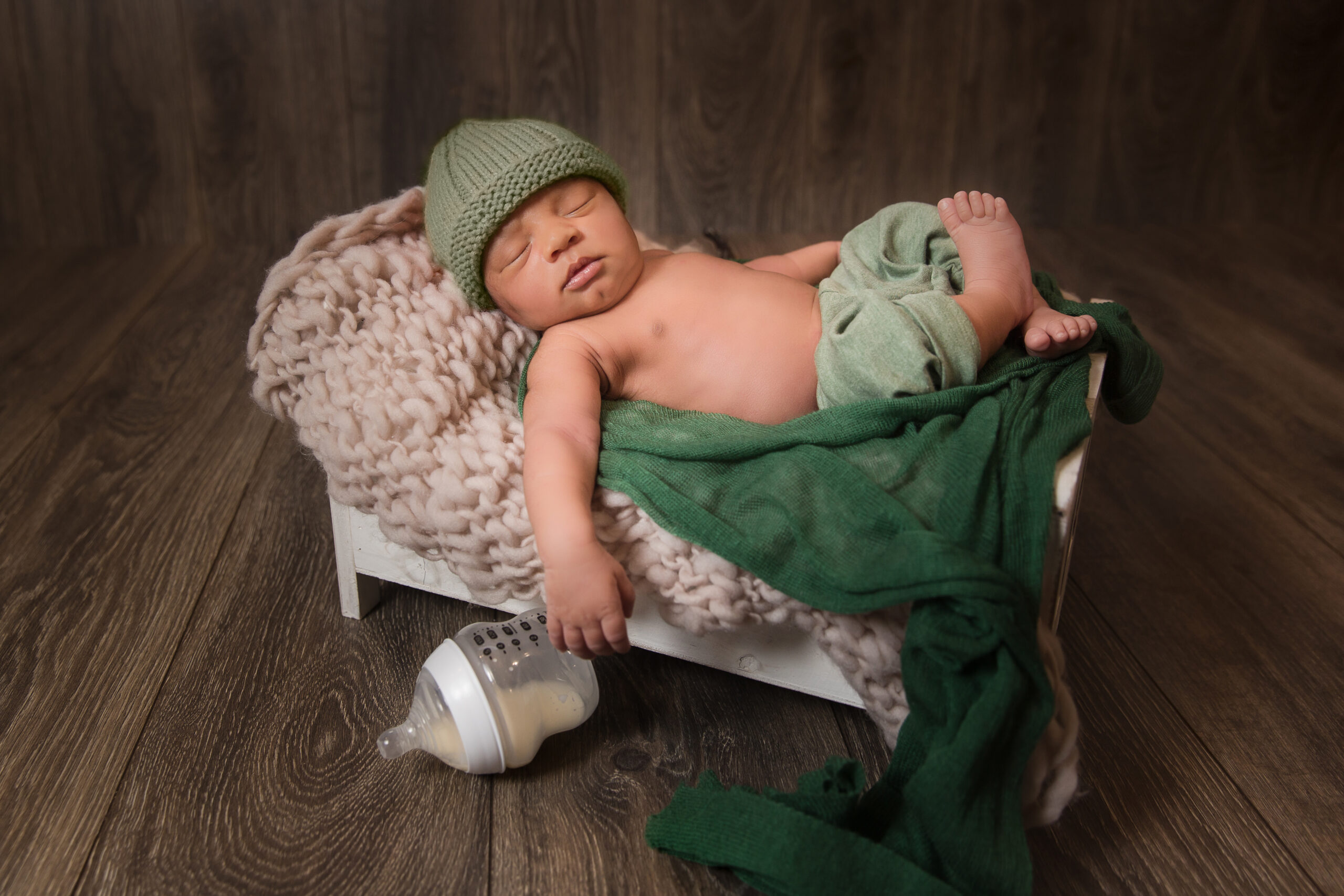 adorable newborn baby boy on bed prop with bottle of milk