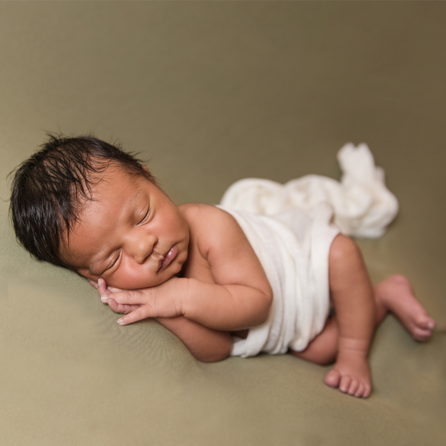 newborn baby in white wrap on sage posing blanket