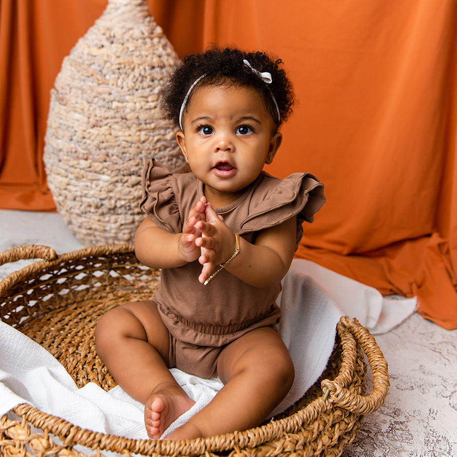 baby girl clapping hands and sitting in basket