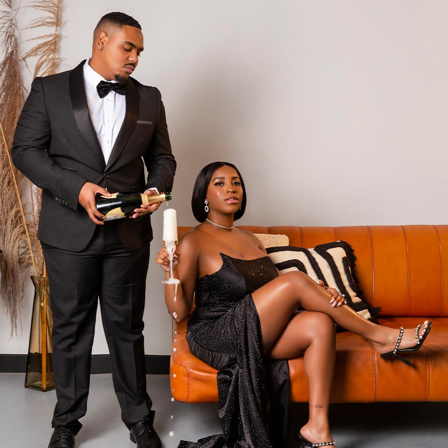 Black couple sitting on couch pouring champagne
