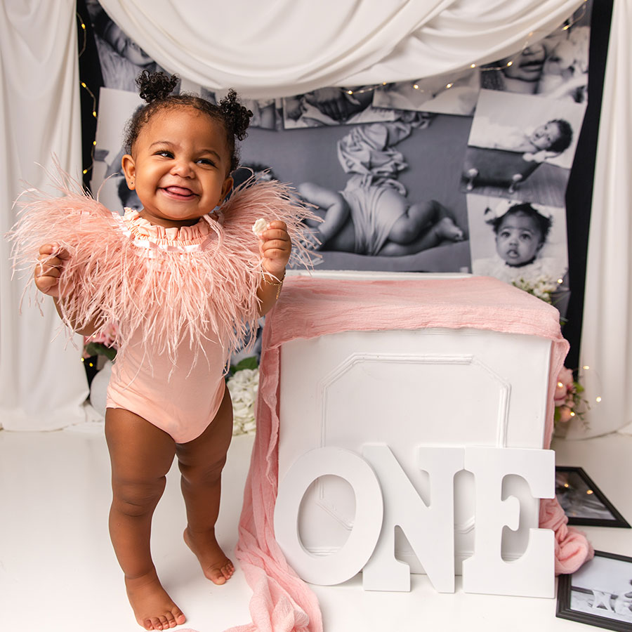 adorable one year old girl with puff balls posing next to first birthday sign